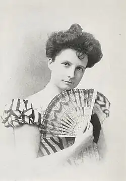 20th-century B&W portrait photo of a woman with her hair in an up-do, wearing a striped, fitted blouse, and holding a fan.