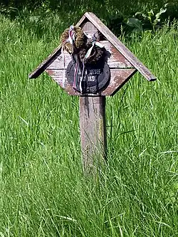 A weathered timber gabled cross grave marker in a grassy meadow.