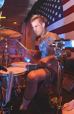 A man plays a drum kit in front of an American flag.