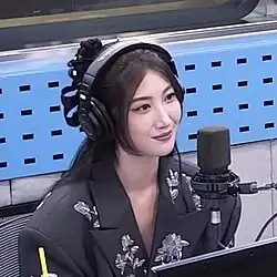 Ejae in a radio recording booth wearing headphones with a microphone near her.