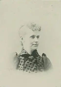 B&W portrait photo of a middle-aged woman wearing a dark, high-collared blouse with her hair in an up-do.