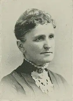19th-century B&W portrait photo of a woman with her hair in an up-do, wearing a dark, fitted blouse.