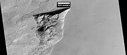 Wide view of triangular depression, as seen by HiRISE. The wall which faces the south pole contains ice in distinct layers that are visible in next image. Location is Hellas quadrangle.[81]
