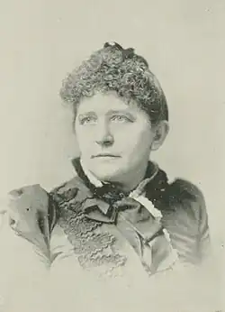 19th-century B&W portrait photo of a woman with her hair in an up-do, wearing a dark, fitted blouse.