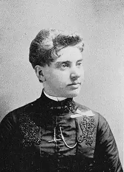 19th-century B&W portrait photo of a woman with her hair in an up-do, wearing a dark, fitted blouse.