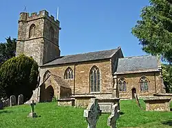 Stone building with square tower. In the foreground are gravestones.