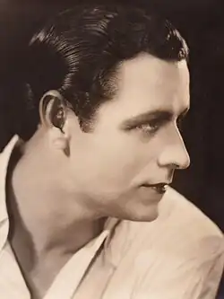 Sepia studio portrait of a clean-shaven man with dark, slicked-back hair, looking to the side