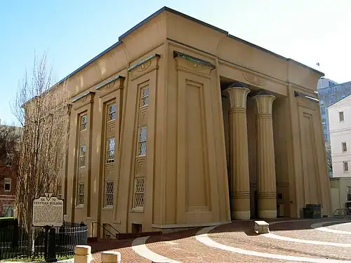 Large tan building in Egyptian Revival style with battered walls, lotus-topped columns, and winged sun disk over entrance