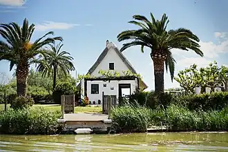 A barraca style construction with greenery around it and a body of water in front of it.