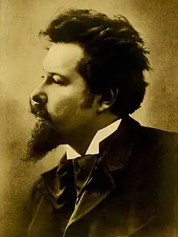 sepia left-profile image of Émile Jaques-Dalcroze wearing a white shirt and dark suit with bowtie, staring ahead intently
