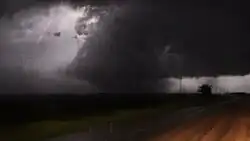 A dark photograph of a large tornado illuminated by a distant lightning flash