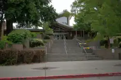 A picture of the front entrance to Inglemoor High School showing trees on the sides with stairs in the middle and the school, semi-modern in the middle