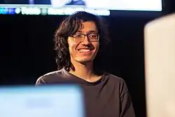 A man with dark brown hair and glasses looking forward and smiling