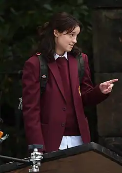 Ramsey wearing a maroon blazer, looking to their left