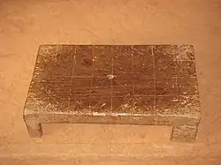 rectangular wooden stool with lines etched into the surface in four rows