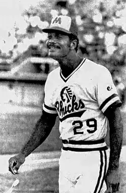 A black and white photo of a man wearing a cap with the insignia of "M" while dressed up in a shirt that has a "CHICKS" wordmark
