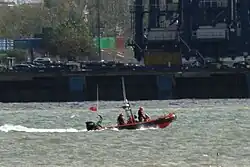 orange and black inflatable boat moving past a quay wall