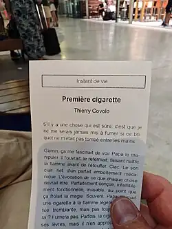 Person holding a small printed French short story booklet titled “Première cigarette” in a public space