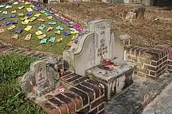 A Chinese grave in a cemetery; there are coloured papers laid around it