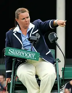 Women in blue blazer sitting on a high green chair with two large microphones in front of her.