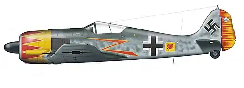 A fighter aircraft, shown in profile, viewed from the left. The aircraft is grey, with a yellow and red nose and a yellow and red rudder at the rear. Decorations include a stylized yellow and red lightning bolt, black-and-white crosses on the body and on the wing, and a black swastika on the tail.