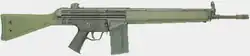 A green Heckler & Koch G3A3 battle rifle lain on a grey background, pointing to the viewer's right