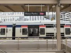 A photo of a railway station with a train passing by. The sign says Rosa PArks SNCF.