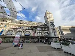 Street-level view of the Gare de Lyon clock tower in Paris, showing the ornate facade and tall clock structure under a bright sky.