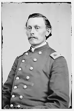 Man with a straight mustache and slick hair combed backward wearing a military uniform with two columns of buttons
