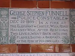 A tablet formed of two large tiles, bordered by green flowers in the style of the Arts and Crafts movement