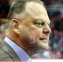 Man standing behind glass at hockey game, in profile