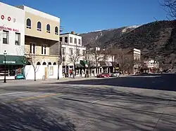 A set of attached two and three-story commercial buildings seen from across a street with a mountain behind them