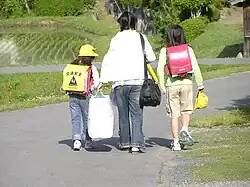 Two sisters wearing pink randoseru. One of them with a yellow plastic cover worn by 1st graders.