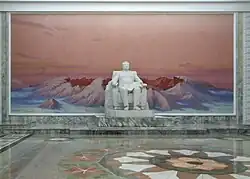 A hallway containing a pure white statue of a sitting middle-aged man, positioned in front of a landscape painting of a mountain.