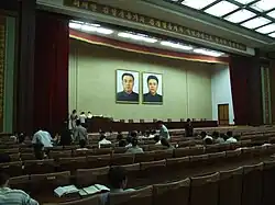 A lecture hall with a large front stand, which two portraits of two men are positioned above.