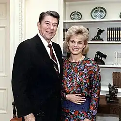 Color portrait of Reagan and Carlson looking at the camera and smiling before an Oval Office wall