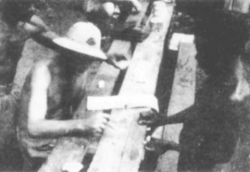 An Australian major, wearing a fiber helmet, pays a local laborer their wages during the Guadalcanal campaign