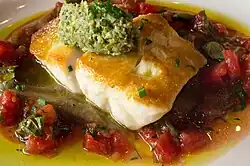 A white fish on a bed of oil topped with sauce vierge and vegetables