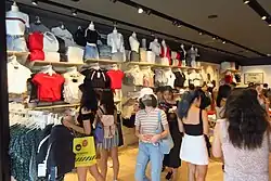 A store with clothes on the wall, full of mostly young women customers