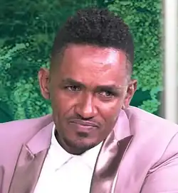 close-up of Hachalu Hundessa wearing a salmon-coloured blazer with white shirt underneath, looking left of camera