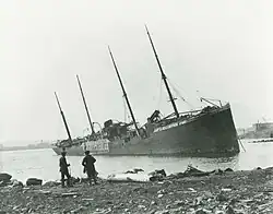 Two men observe a large beached ship with "Belgian Relief" painted on her side