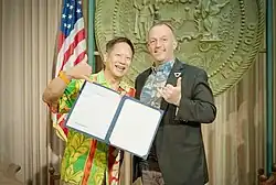 Steve Sue and Governor Josh Green hold a signed document and make the shaka gesture