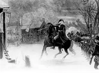 Black and white print shows George Washington on horseback leading his soldiers and pointing with his sword. The combat is taking place on a town street with Hessian soldiers visible in the background.
