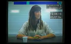 Desktop footage of woman sitting at a police interview desk. Subtitle reads "Please."