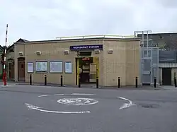 A beige-bricked building with a rectangular, blue sign reading "HIGH BARNET STATION" in white letters all under a blue sky with white clouds