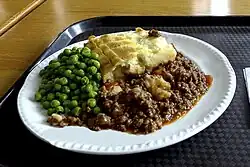 Photograph of a dinner plate on which a helping of minced meat topped with mashed potato, served alongside peas.