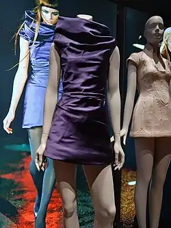 Left, a purple minidress with a high, wide neck. Right, a flesh-toned micro-minidress with raised lines in a pattern and high collar open at the front to show decolletage.