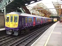 A commuter train at a station. Below the train, four rails are visible—two are for the wheels and one provides power. Above the train, a catenary power line is also visible.