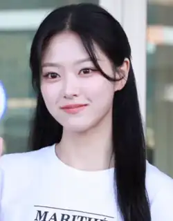 A young Asian woman with long black hair and brown eyes wearing a white t-shirt smiling while looking off into the distance.