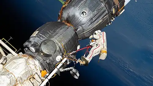 A cosmonaut inspecting the exterior of a spacecraft during a spacewalk; Earth appears in the background